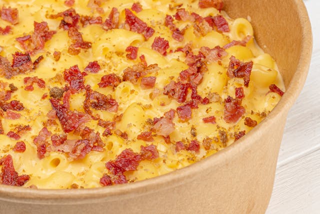 Close-up of a one-pan cheesy cheeseburger rice skillet with ground beef, rice, and garnished with green onions, alongside raw bacon slices and a pot of cheesy sauce.