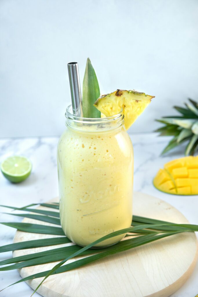 Glass of tropical smoothie made with mango, pineapple, papaya, and banana, served chilled with a garnish of lime.
