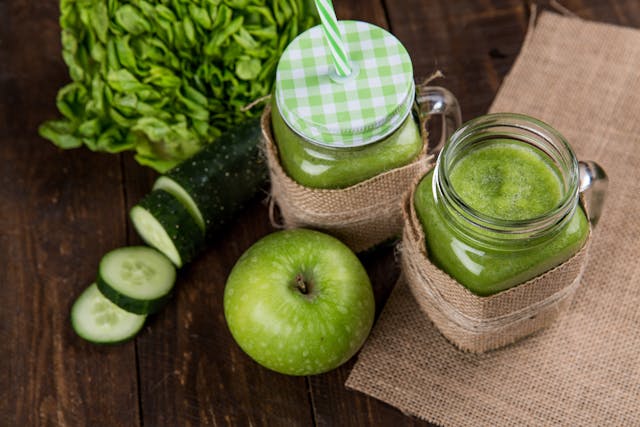 Two glasses of a refreshing green smoothie with an apple, and a cucamber over a table