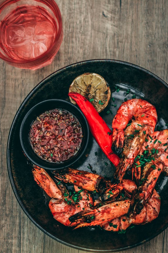 A close-up on a balck plate of golden honey garlic shrimp with a small bowl of hot sauce.