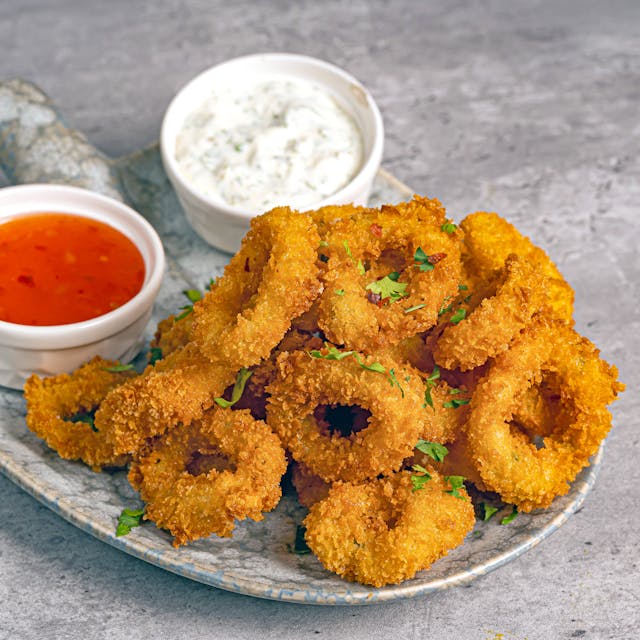 A close-up look of a golden fried calamari rings with two little bowls of sauce.
